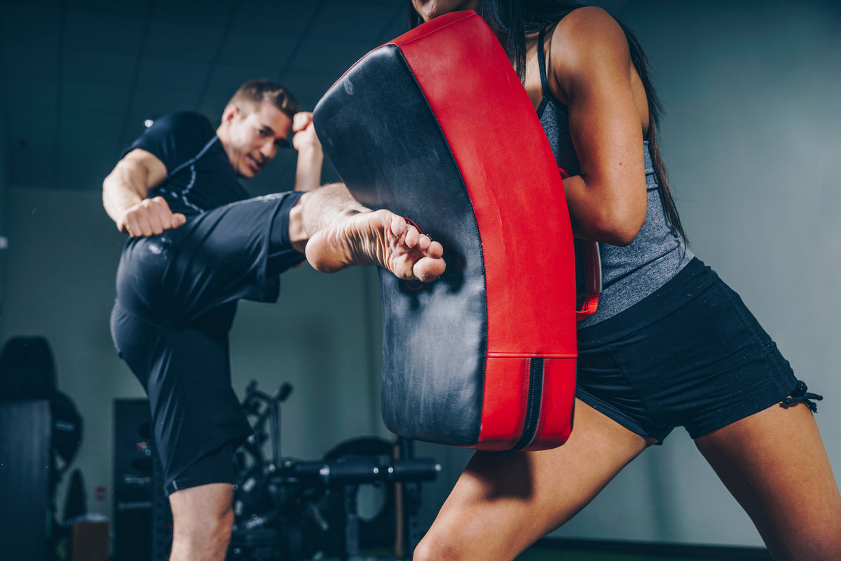 MMA fighter delivering powerful kick to pad wearing STRYK training gear - combat strength apparel.